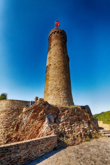 Rond stenen toren op een rots met een vlag bovenop, tegen een heldere blauwe lucht.