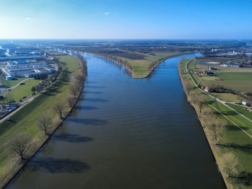 Een brede rivier met groene oevers en bomen onder een heldere blauwe lucht.