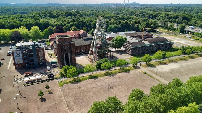 Luchtfoto van een verlaten industrieterrein met groene bomen en oude gebouwen.