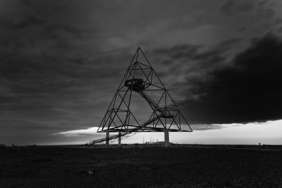 Zwart-wit afbeelding van een grote, open driehoekige structuur onder een dreigende lucht.