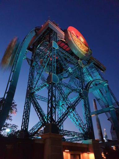 Groot draaiend rad met kleurrijke verlichting tegen een nachtelijke achtergrond.