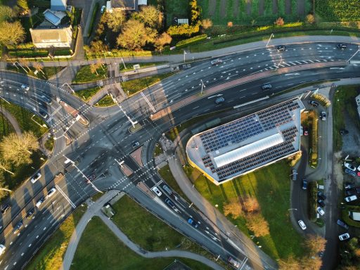 Luchtfoto van een druk verkeersknooppunt met een gebouw en parkeerplaats.