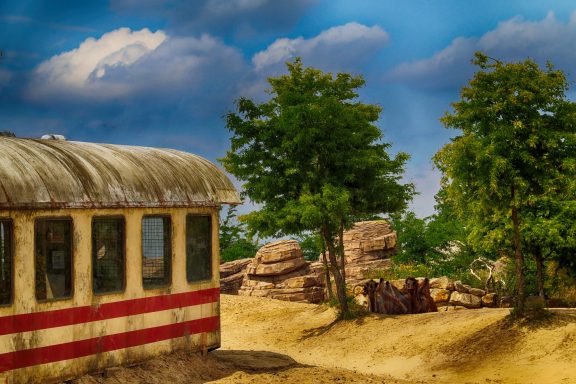 Besloten landschap met een oude treinwagon en rotsen, omringd door groene bomen.