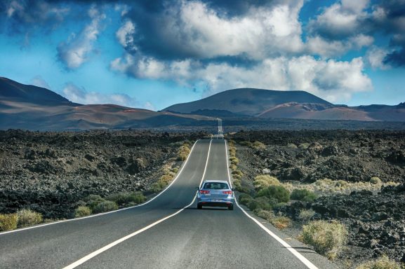 Een auto rijdt over een rechte weg door een woestijnachtig landschap met bergen.