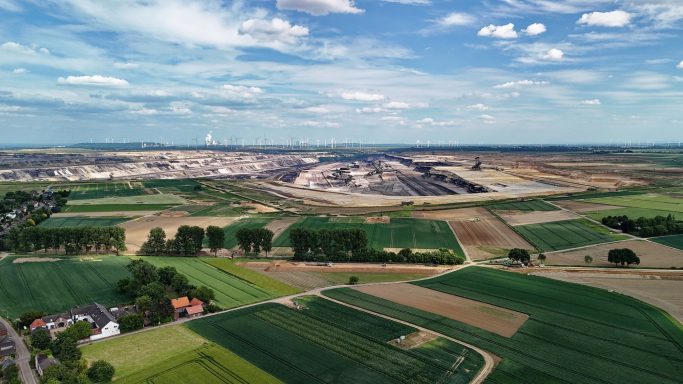 Landschap met velden, bomen en een kleigroeve op de achtergrond onder een heldere lucht.