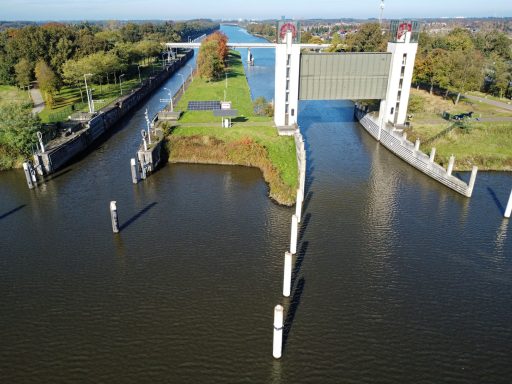 Schutsluis met een brede waterweg en groene oevers, omringd door bomen.