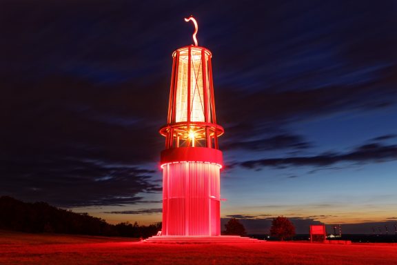 Rood verlichte vuurtoren tegen een donkere lucht tijdens de schemering.