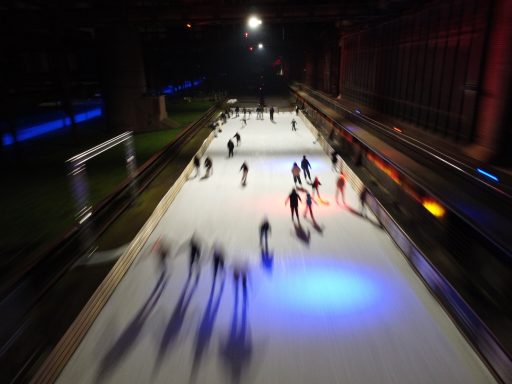 Schaatsers op een verlichte ijsbaan onder een donkere hemel.