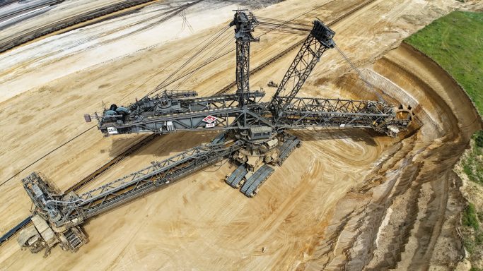 Bovenaanzicht van een grote graafmachine op een zandachtige werklocatie.