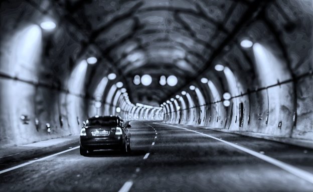 Zwart-wit foto van een auto die een tunnel binnengaat met verlichting langs de wanden.