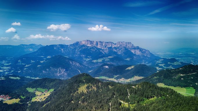 Uitgestrekt berglandschap met groene valleien en blauwe lucht.