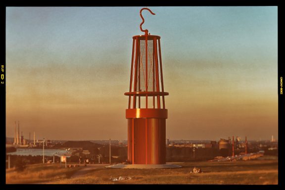 Rode toren met haak op een heuvel bij zonsondergang, uitzicht op industriegebied.