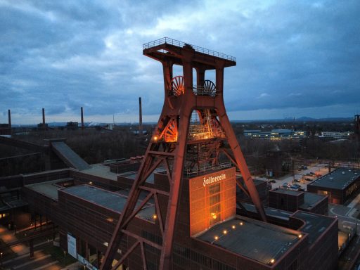 Een oude mijnschacht met een opvallende rode lift, omgeven door een industriële omgeving.