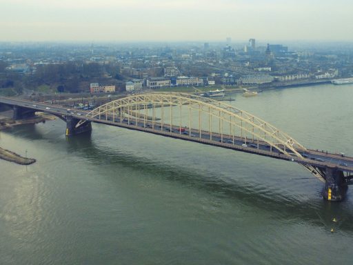 Een grote, boogvormige brug over een rivier met een stedelijke achtergrond.